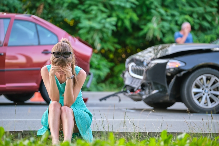 Sad female driver sitting on street side shocked after car accident.